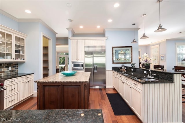 kitchen with a kitchen bar, sink, tasteful backsplash, built in appliances, and decorative light fixtures