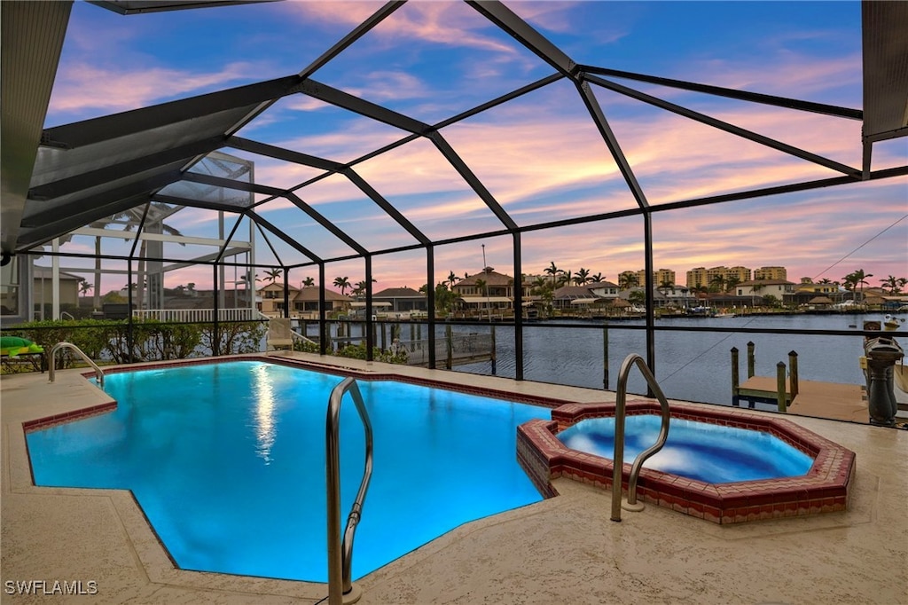 pool at dusk with a water view, an in ground hot tub, a lanai, and a patio area