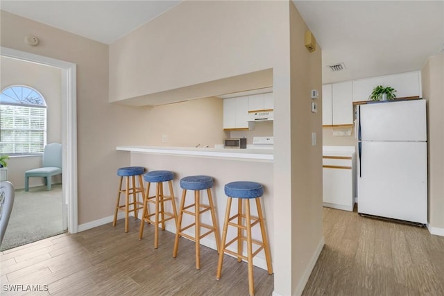 kitchen featuring white refrigerator, light hardwood / wood-style flooring, a kitchen bar, white cabinetry, and extractor fan