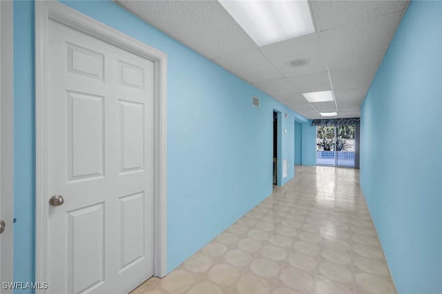 hall with a paneled ceiling and tile patterned floors