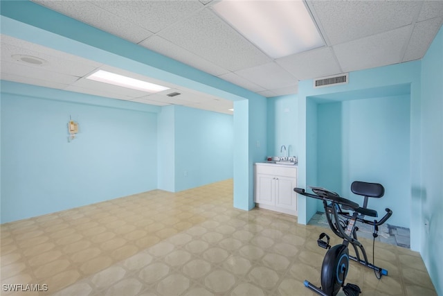 workout area with visible vents, a sink, a drop ceiling, and light floors