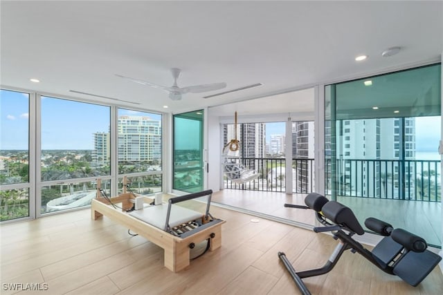 exercise room with ceiling fan, a wealth of natural light, a wall of windows, and light hardwood / wood-style flooring