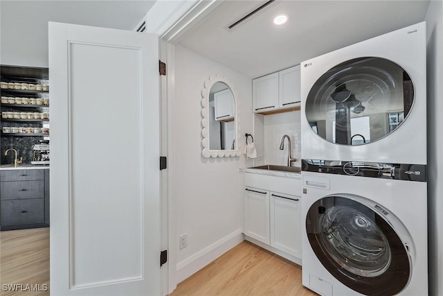 laundry room featuring stacked washer / dryer, sink, cabinets, and light hardwood / wood-style floors