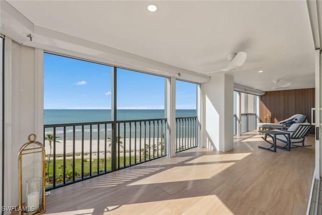 sunroom / solarium featuring a water view, ceiling fan, and a beach view