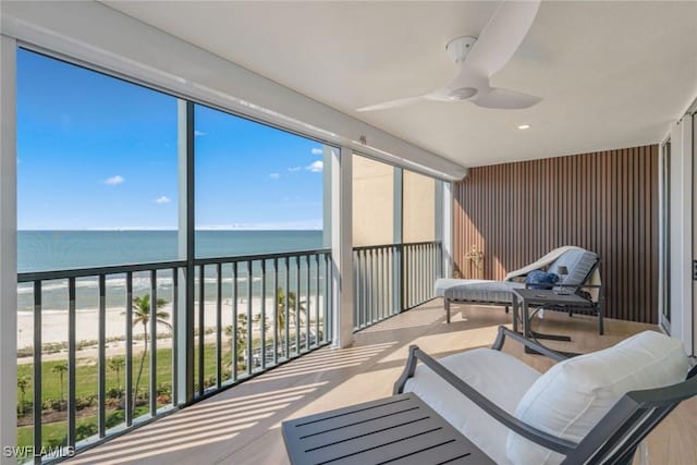 sunroom featuring ceiling fan, a water view, and a view of the beach