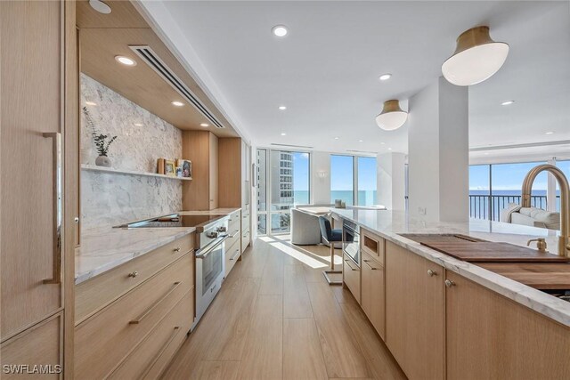 kitchen with light brown cabinetry, light wood-type flooring, a water view, expansive windows, and high end stove