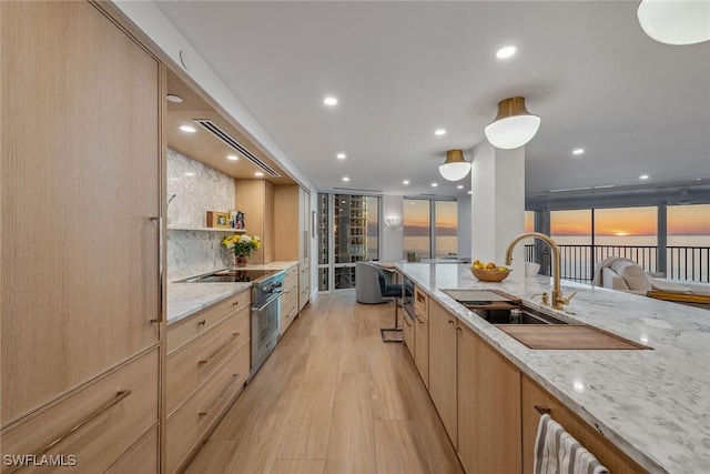 kitchen with light brown cabinets, sink, light stone countertops, high end stainless steel range oven, and light hardwood / wood-style floors