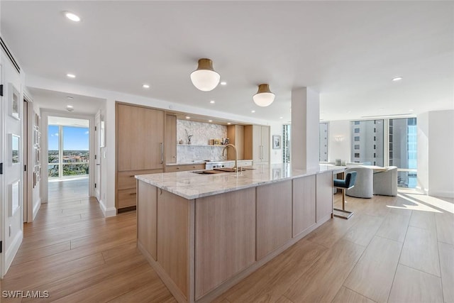 kitchen featuring light stone countertops, a large island with sink, light brown cabinets, sink, and light hardwood / wood-style flooring