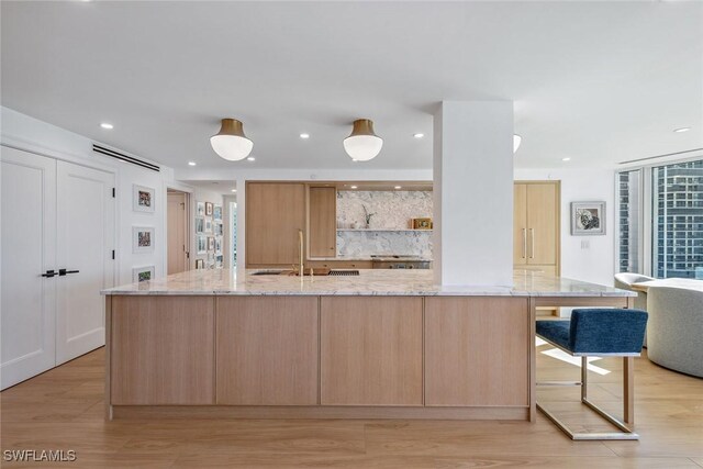 kitchen featuring tasteful backsplash, a large island, sink, light stone counters, and light brown cabinets