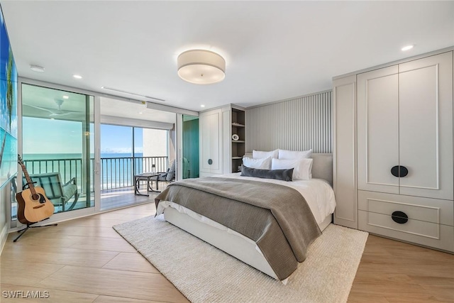 bedroom with a wall of windows, light wood-type flooring, a water view, and access to outside