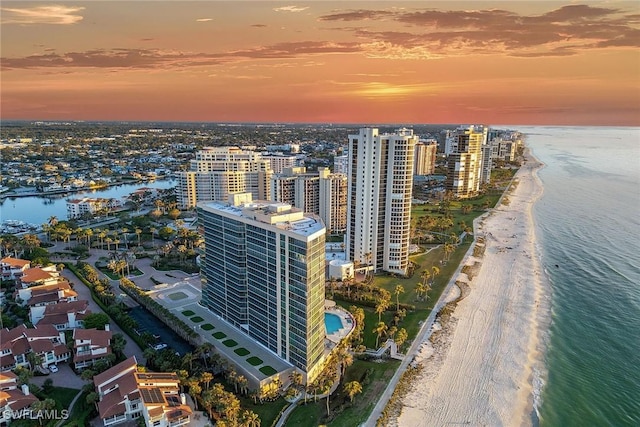 aerial view at dusk featuring a water view and a view of the beach