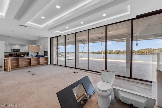 living room featuring a raised ceiling, expansive windows, and a water view