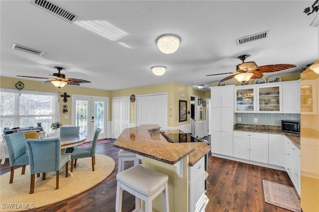 kitchen with a breakfast bar, backsplash, black appliances, white cabinets, and dark hardwood / wood-style flooring