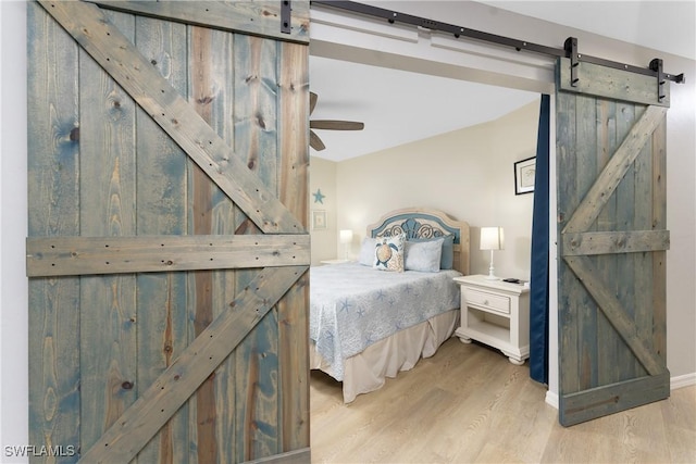 bedroom with a barn door, ceiling fan, and hardwood / wood-style flooring