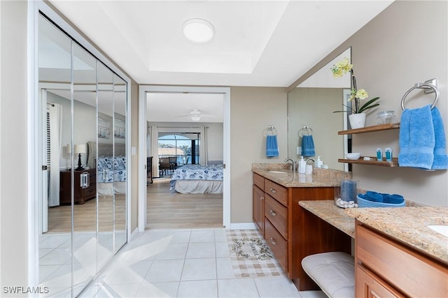 bathroom featuring a skylight, vanity, a raised ceiling, ceiling fan, and tile patterned flooring