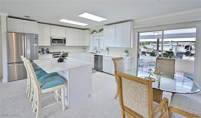 kitchen with white cabinets, light carpet, a center island, and stainless steel appliances