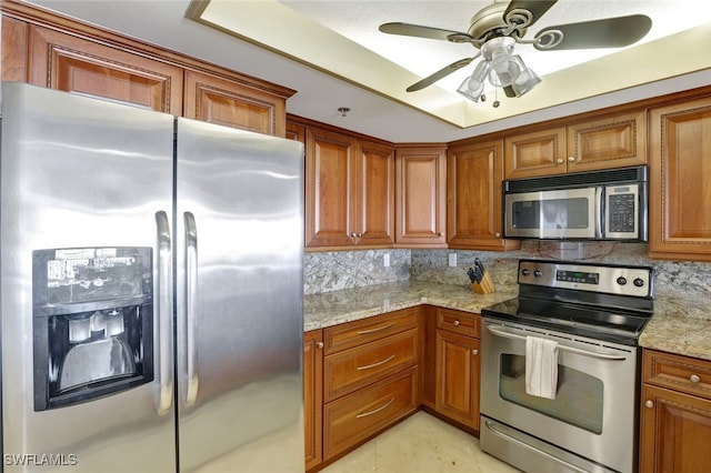 kitchen with light stone countertops, appliances with stainless steel finishes, decorative backsplash, a raised ceiling, and light tile patterned floors