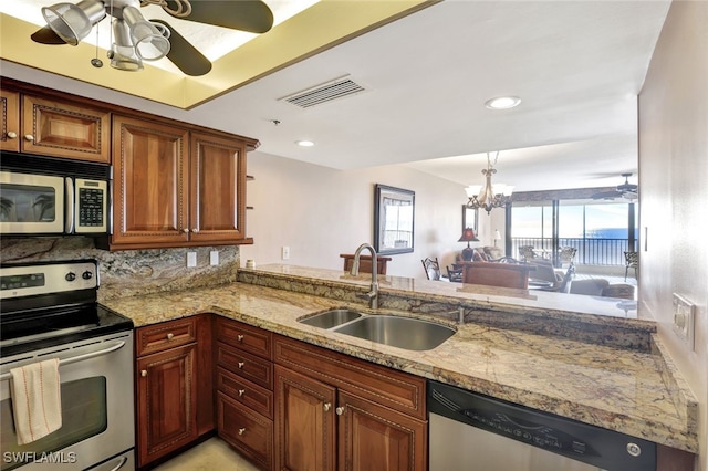 kitchen with kitchen peninsula, appliances with stainless steel finishes, decorative backsplash, light stone countertops, and sink