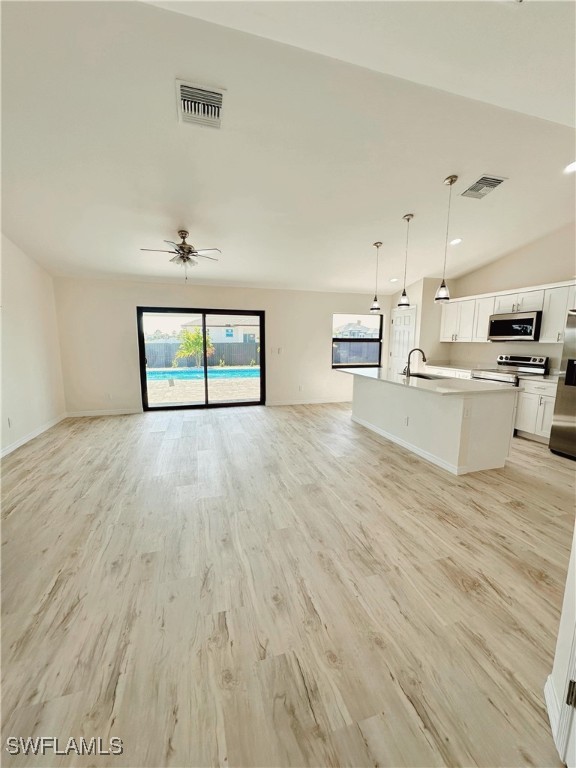 unfurnished living room with ceiling fan, sink, vaulted ceiling, and light wood-type flooring