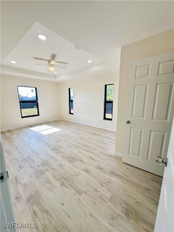 empty room with light wood-type flooring, a raised ceiling, and ceiling fan