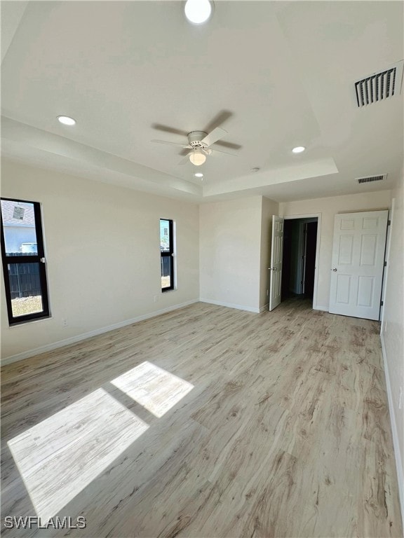 unfurnished room with light hardwood / wood-style flooring, a raised ceiling, and ceiling fan