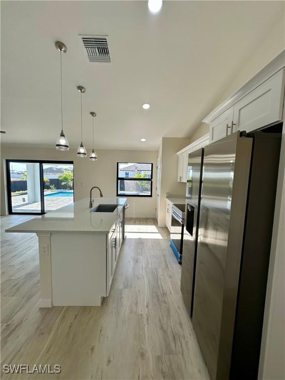 kitchen with sink, hanging light fixtures, stainless steel fridge, an island with sink, and white cabinets