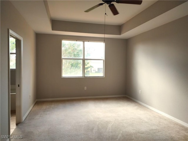 carpeted spare room with ceiling fan, a raised ceiling, and a wealth of natural light