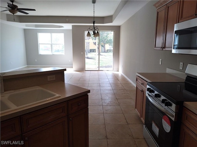 kitchen with appliances with stainless steel finishes, ceiling fan with notable chandelier, a raised ceiling, sink, and light tile patterned floors