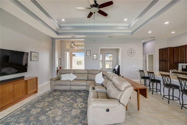 living room with a raised ceiling, ceiling fan, light tile patterned flooring, and ornamental molding