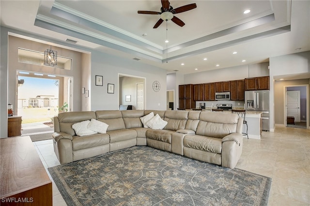 living room featuring a raised ceiling, a towering ceiling, ceiling fan with notable chandelier, and ornamental molding