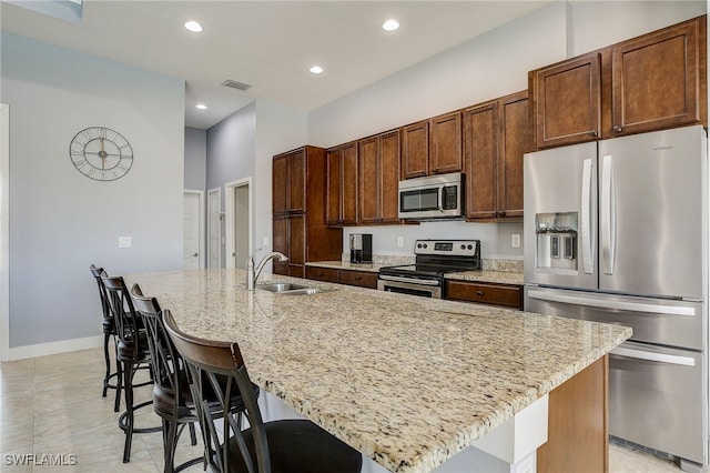 kitchen with appliances with stainless steel finishes, a kitchen breakfast bar, light stone counters, sink, and a center island with sink