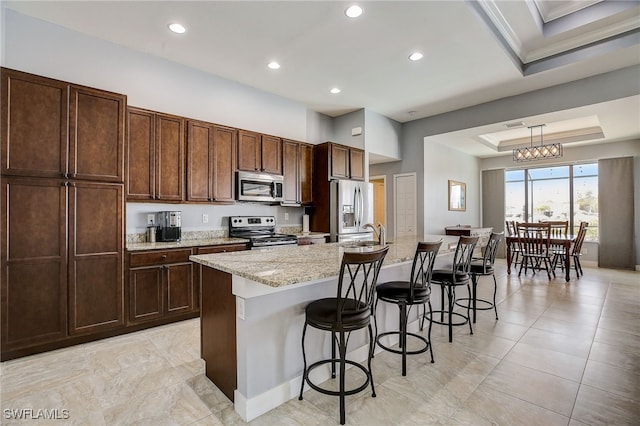 kitchen featuring pendant lighting, a kitchen island with sink, an inviting chandelier, appliances with stainless steel finishes, and a tray ceiling