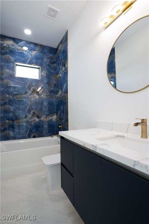 full bathroom featuring vanity, tiled shower / bath combo, and toilet