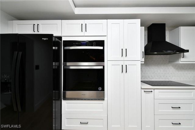 kitchen with decorative backsplash, white cabinetry, black appliances, and wall chimney range hood