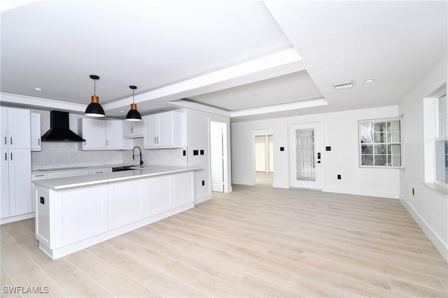 kitchen featuring sink, wall chimney exhaust hood, decorative light fixtures, a tray ceiling, and white cabinets