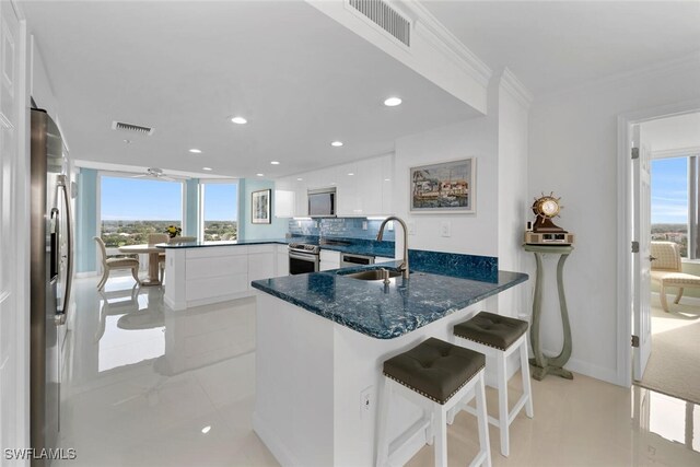 kitchen with appliances with stainless steel finishes, kitchen peninsula, a kitchen bar, white cabinets, and sink