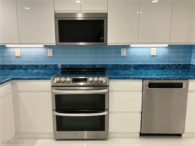 kitchen with stainless steel appliances, decorative backsplash, white cabinetry, and dark stone countertops