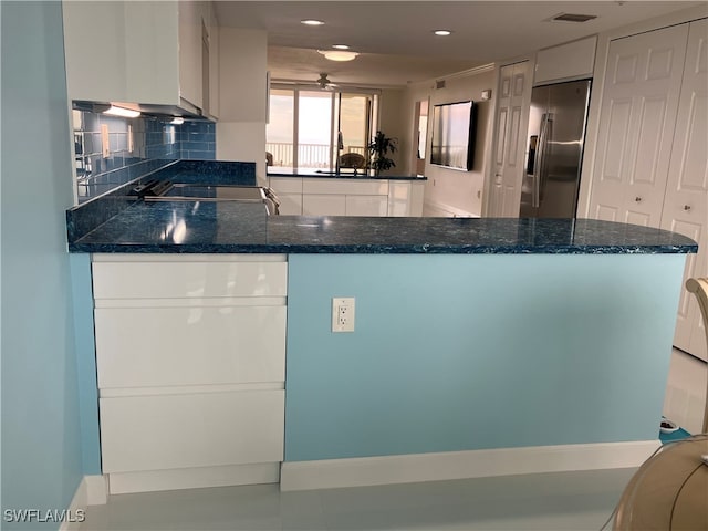 kitchen with stainless steel fridge with ice dispenser, black electric stovetop, backsplash, white cabinets, and dark stone counters