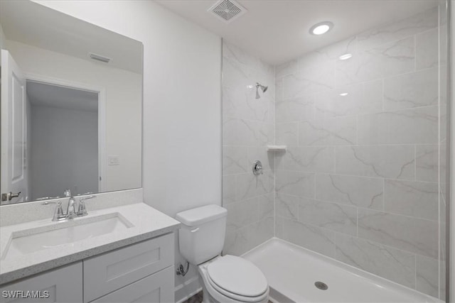 bathroom featuring a tile shower, vanity, and toilet