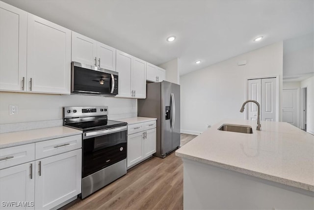 kitchen with white cabinets, sink, light stone countertops, light wood-type flooring, and appliances with stainless steel finishes