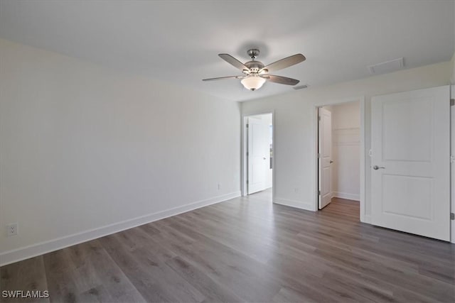 unfurnished bedroom with a walk in closet, a closet, ceiling fan, and dark wood-type flooring