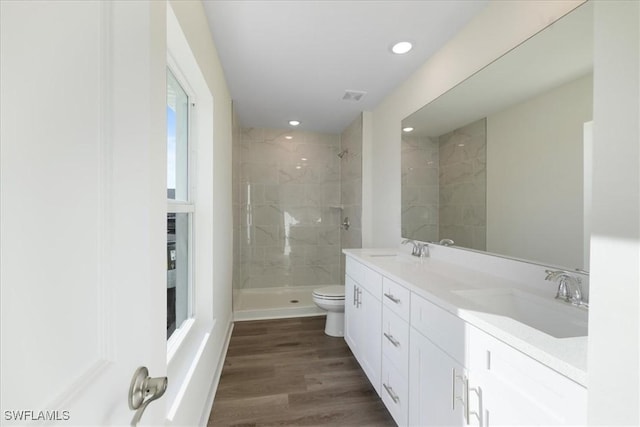 bathroom featuring a tile shower, toilet, vanity, and hardwood / wood-style flooring