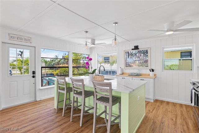 kitchen featuring pendant lighting, a breakfast bar, white cabinetry, a center island with sink, and light wood-type flooring