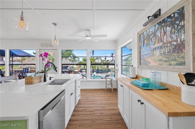 kitchen featuring pendant lighting, white cabinetry, dishwasher, sink, and light stone counters