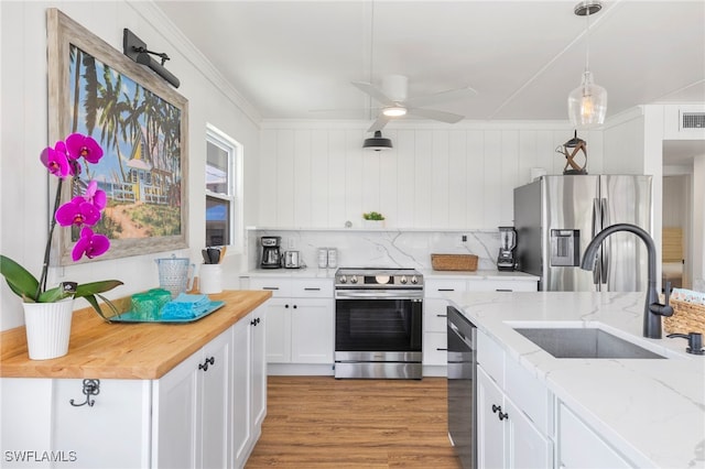 kitchen featuring sink, white cabinetry, appliances with stainless steel finishes, pendant lighting, and light stone countertops