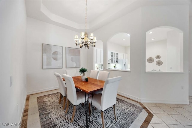 dining area with a raised ceiling, light tile patterned flooring, and an inviting chandelier