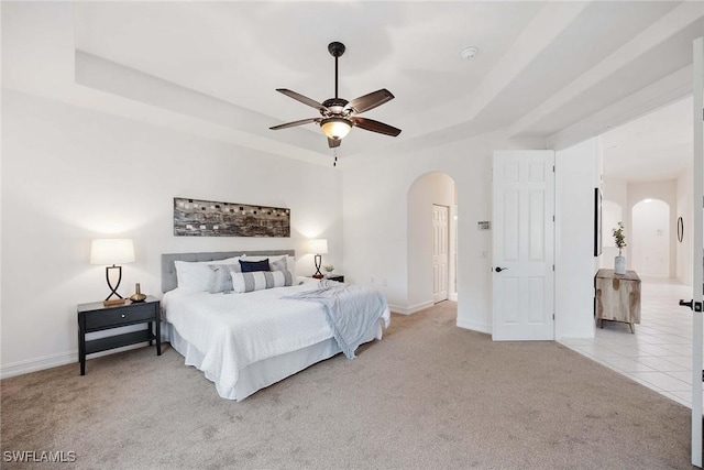 bedroom featuring light colored carpet, a raised ceiling, and ceiling fan