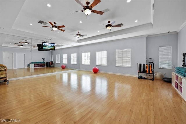 exercise area with a raised ceiling, light hardwood / wood-style floors, and ornamental molding