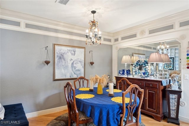 dining space with crown molding, light wood-type flooring, and a notable chandelier