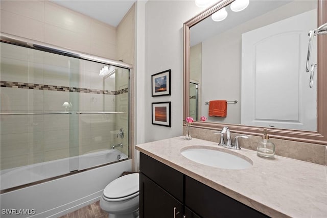 full bathroom with combined bath / shower with glass door, wood-type flooring, vanity, and toilet